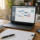 Mesa de home office com notebook, agenda, celular e balança da justiça para artigo sobre horas extras no teletrabalho